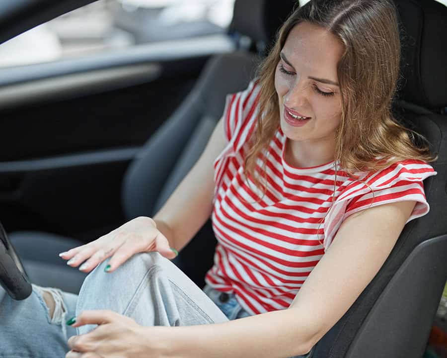 Young woman with knee pain sitting in her car after an accident