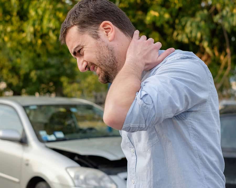 Man feeling neck pain after a car accident, wrecked vehicle in the background