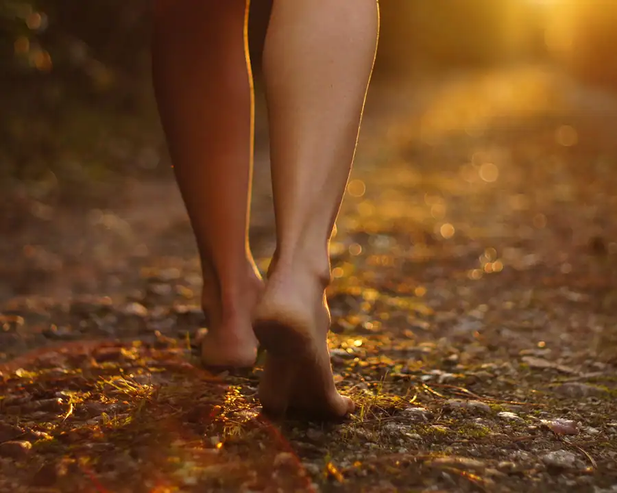 lady walking barefoot on a dirt road into the sunset