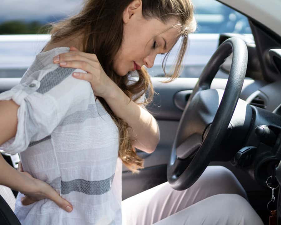 lady in her car rubbing her shoulder and back pains