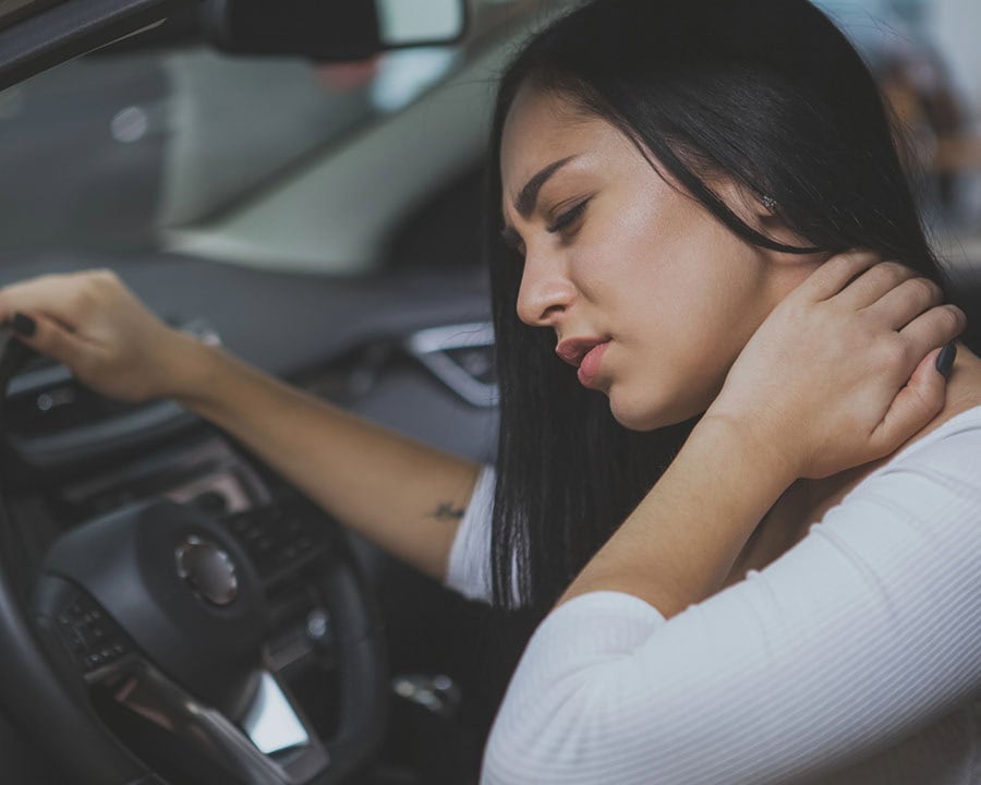 lady in her car holding the steering wheel and rubbing her sore neck