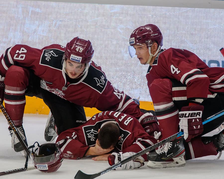 two ice hockey player help their fallen team mate up off the ice