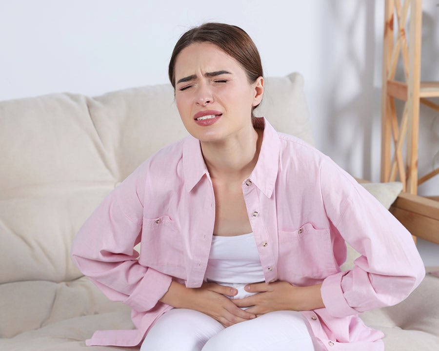 Young woman experiencing pelvic pain on sofa at home