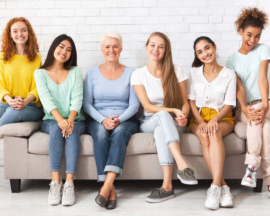 Mutiracial Ladies Of Different Age Sitting On Couch Posing And Smiling Together