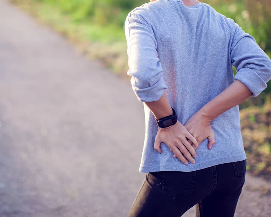 woman suffering from hip pain at the back, while running outdoors