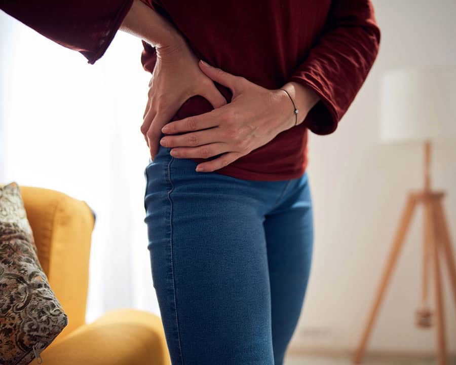 Woman in jeans with strong hip pain at home.