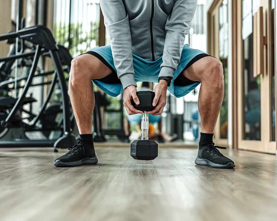 A man doing squat exercises with dumbbell at gym. Fitness, workout and training concept.