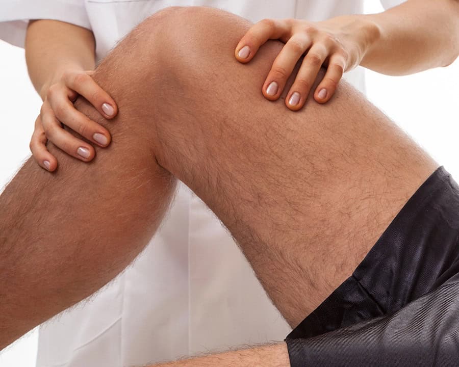 physical therapist's hands diagnosing patient with painful knee